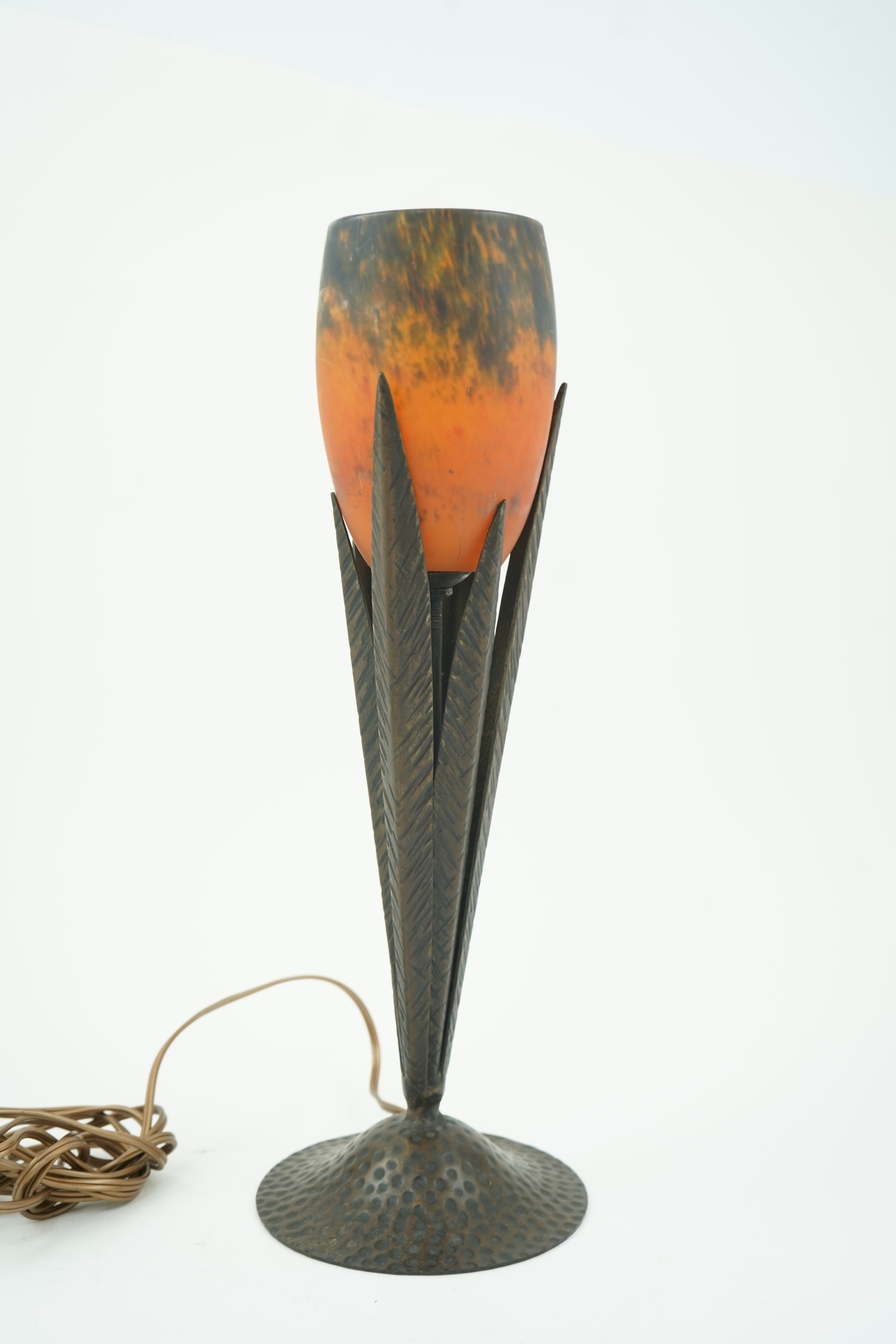 Manner of Muller Freres and Robj: A French Art Deco table lamp the mottled orange glass shade supported by naturalistic palm-leaf metal supports terminating in a circular hammered metal base, 40cm high